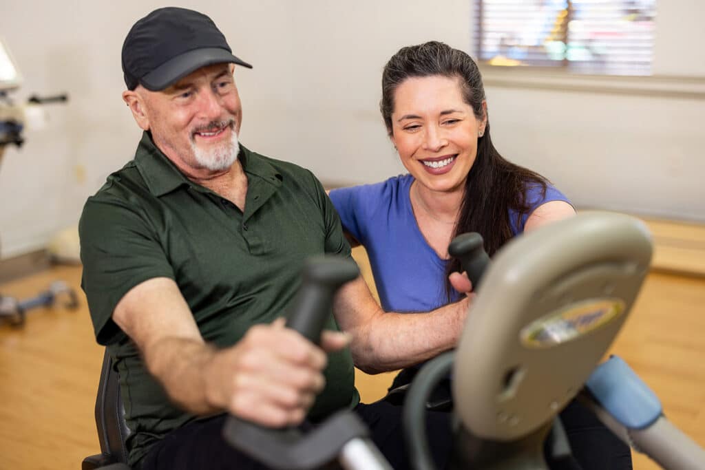 Physical therapist assisting patient on bike in rehab gym at Ahwatukee Post Acute